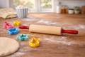 Rolling pin with colorful cookie cutters on a wooden surface with flour.