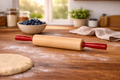 Wooden rolling pin with red handle on a wooden table with flour, blueberries, and a bowl in the background.
