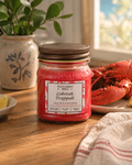 Red candle labeled 'Lobstah Trappah' by Fletcher's Mill on a wooden table with a lobster and lemon in the background.