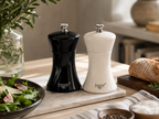 Black and white pepper mills on a table with a salad and bread