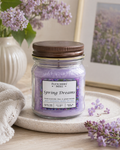 Jar of 'Spring Dreams' candle from Fletchers Mill on a surface with flowers and a towel in the background.