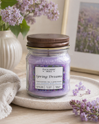 Jar of 'Spring Dreams' candle from Fletchers Mill on a surface with flowers and a towel in the background.