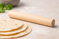 Wooden rolling pin next to tortillas on a light surface