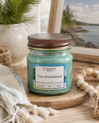 Jar candle labeled 'Vacationland' by Fletchers Mill on a wooden surface with a scenic background.